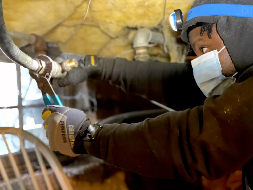 Gas line installation beneath a floor, with a worker using a wrench